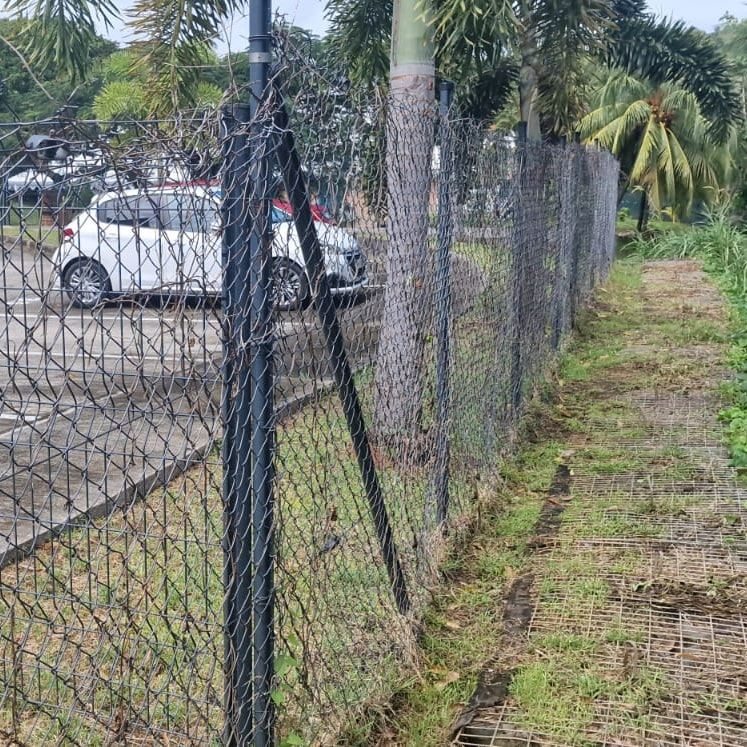 Clôture en grillage retendue et renforcée par une jambe de force en diagonale, le long d'un parking